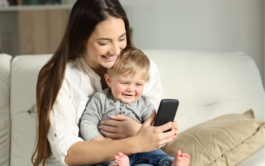 Child sitting on mother's lap smiling at the phone the mother is holding