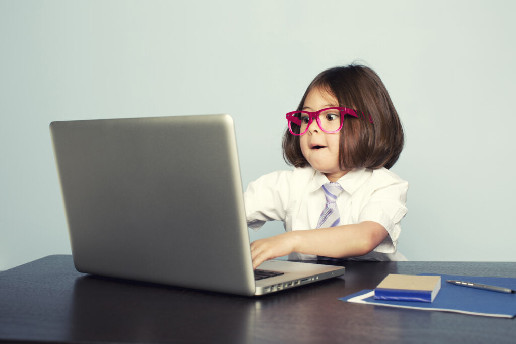 A young girl with glasses types excitedly on a laptop