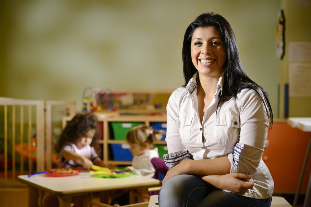 A teacher sitting in a room while children play behind her
