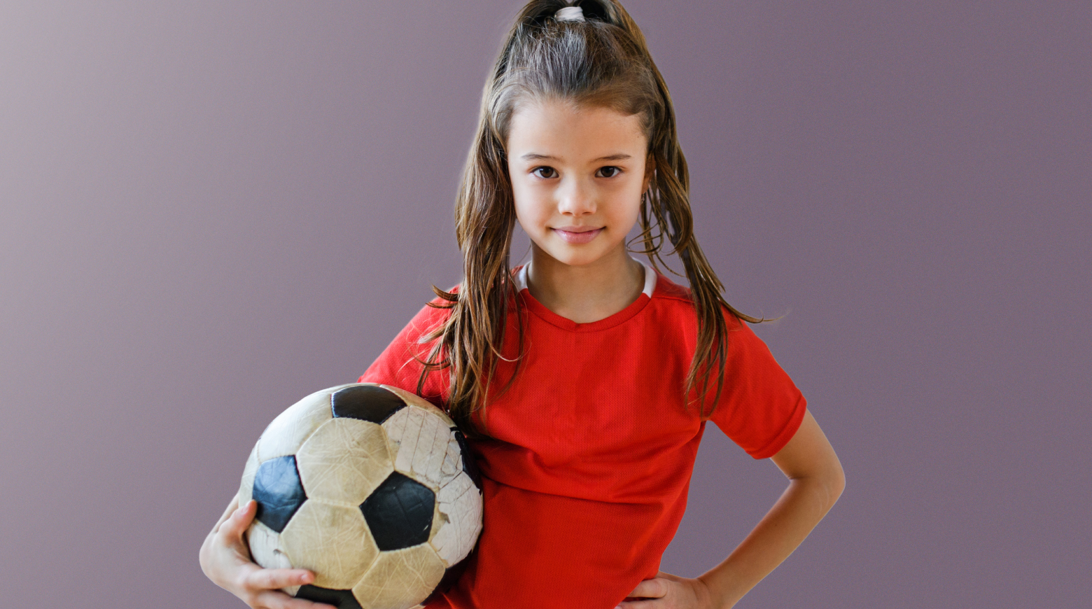 A young girl wearing a red top holding a soccer ball