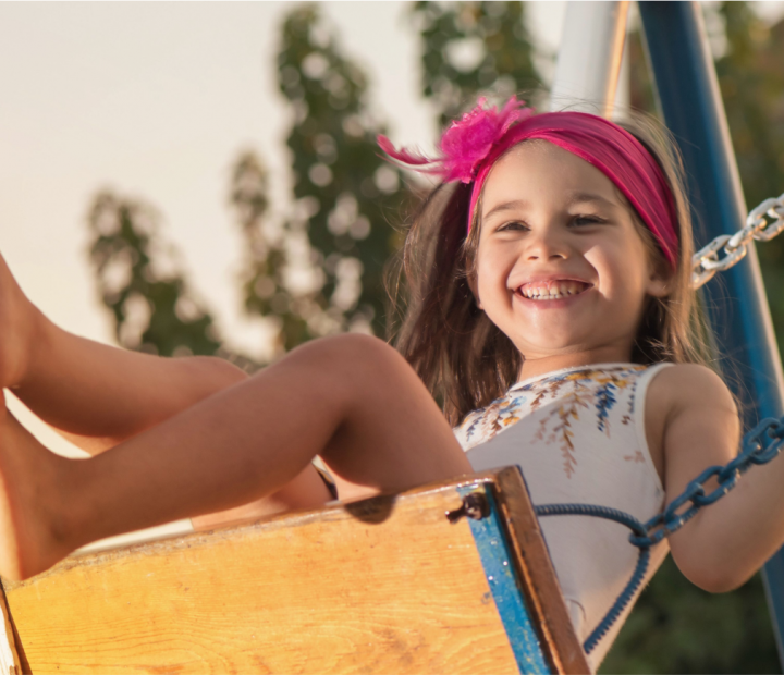 A picture of a young girl swinging on a swing with a huge smile on her face