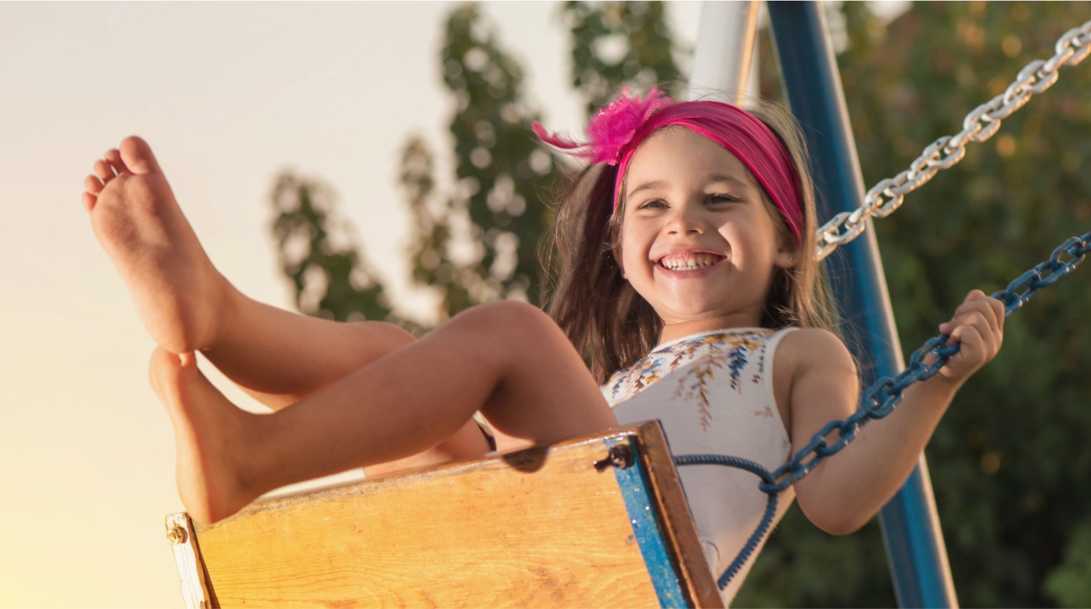A picture of a young girl swinging on a swing with a huge smile on her face