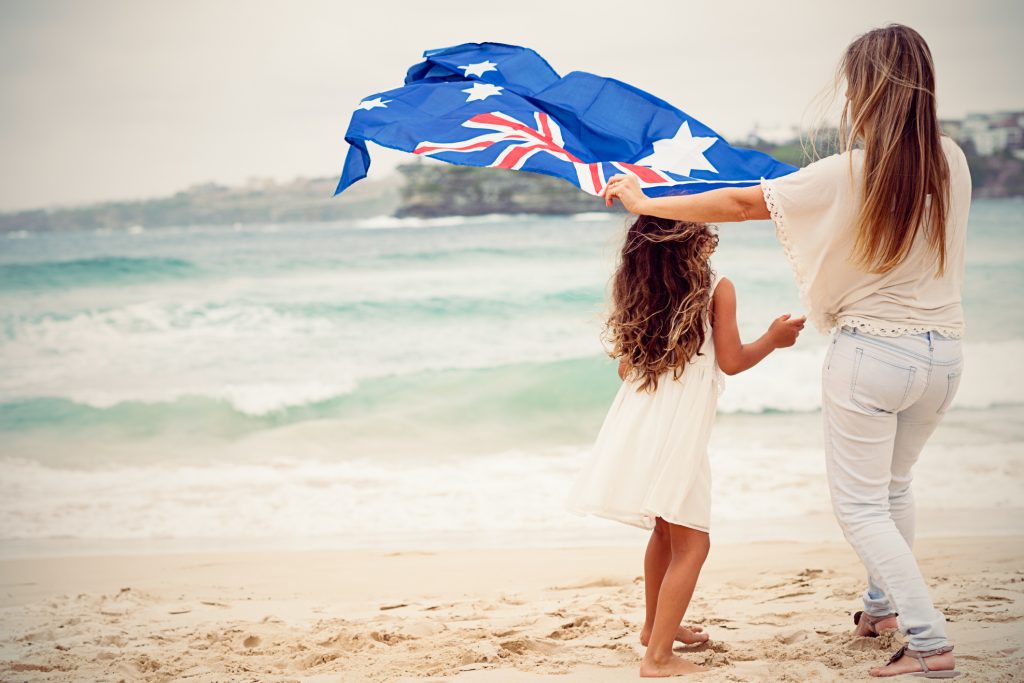 A mother holding the Australian flag over her daughter’s head on the beach