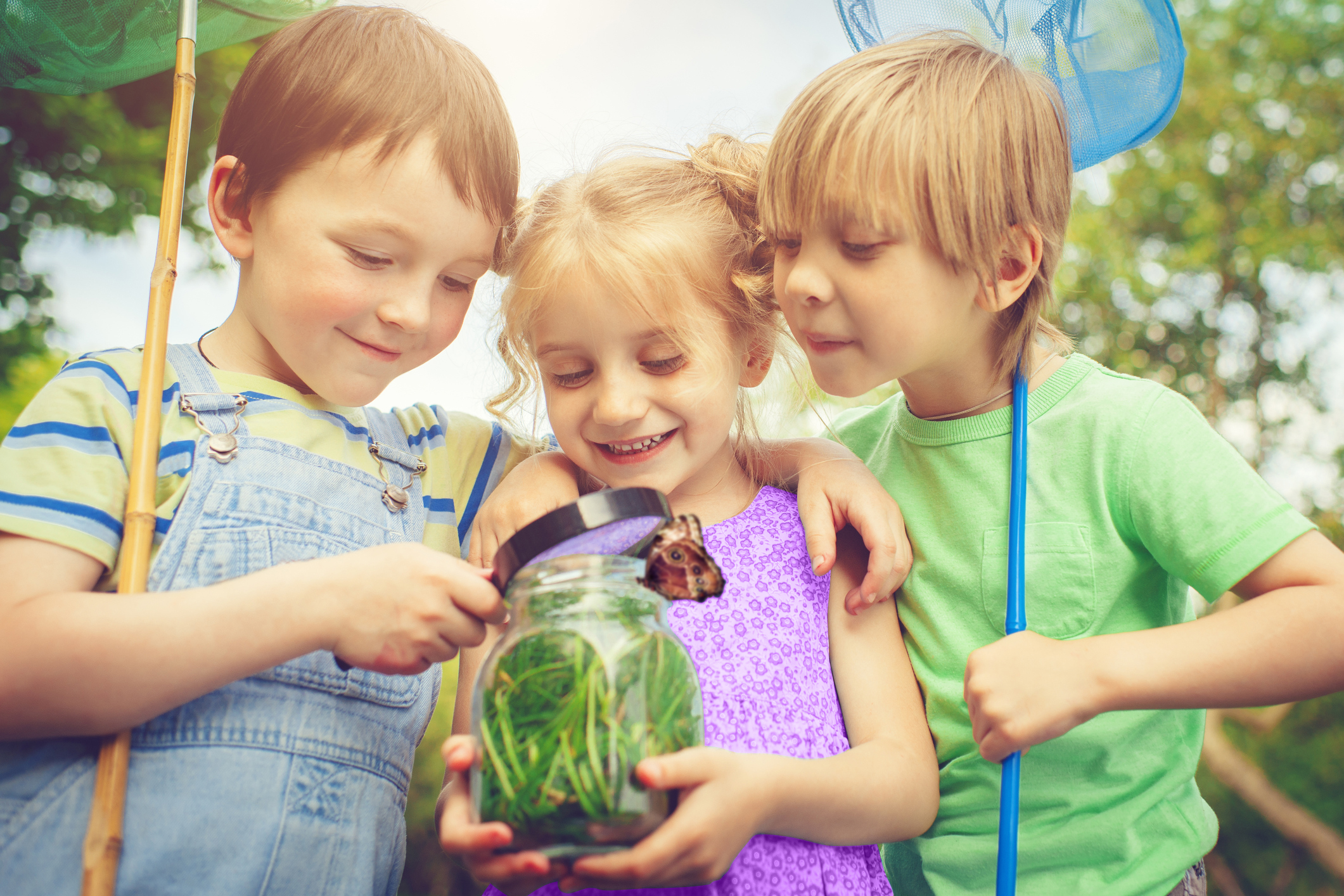 Three children engaging in outdoor play while looking at insects in a jar