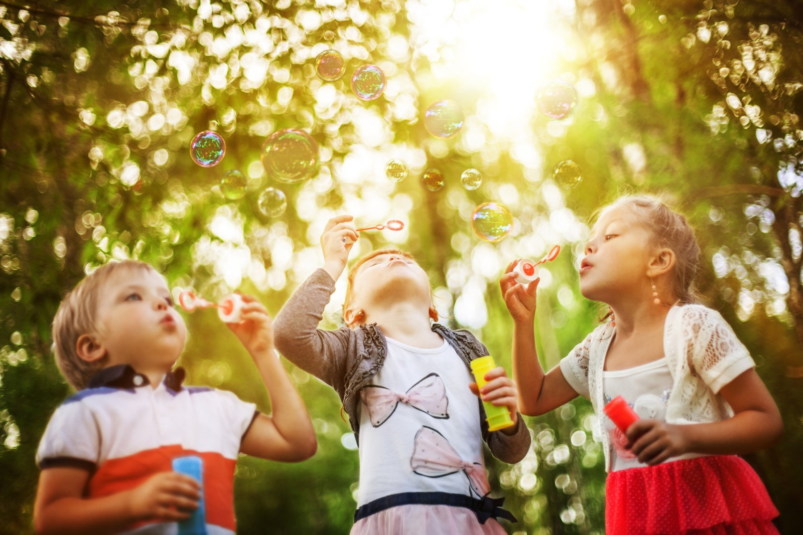 Three children engaging in outdoor play by blowing bubbles