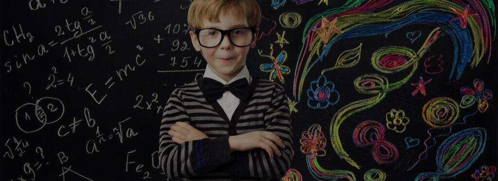 A young boy with glasses and a bow tie standing in front of a blackboard filled with mathematical formulas
