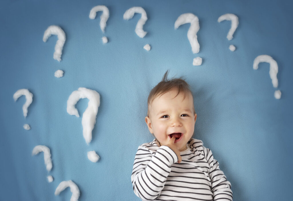 A young chid with a finger in his mouth against a light blue background with several question marks made from cotton