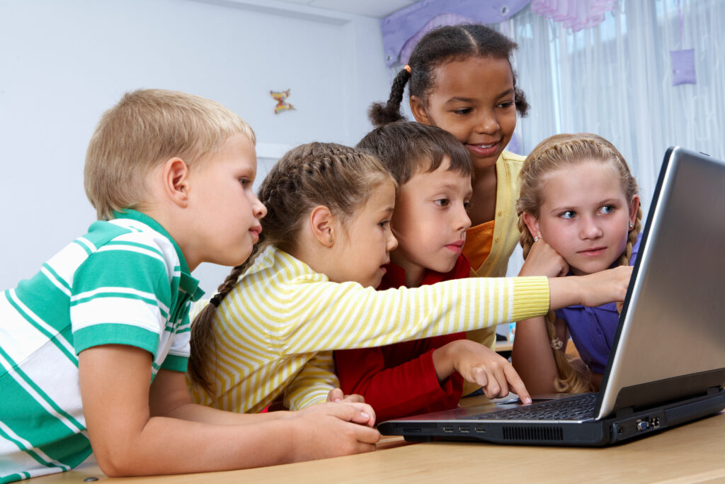 Children gathered around a laptop, pointing at the screen.
