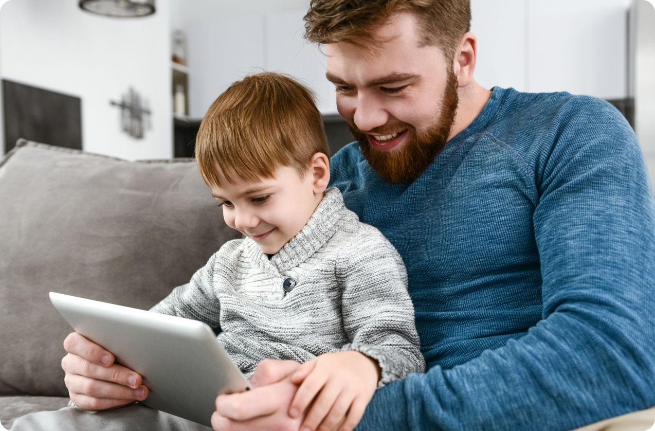 Young boy sitting on father's lap looking at a tablet