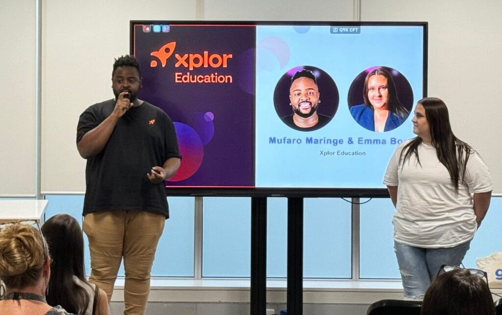 Male and female presenters stand in front of a display showing Xplor Education, provider of childcare educator platforms