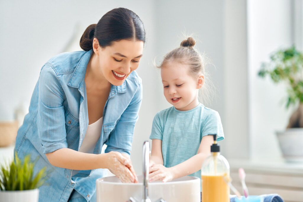 A woman and young girl washing their hands, one of the good hygiene practices you can implement at your wraparound care setting