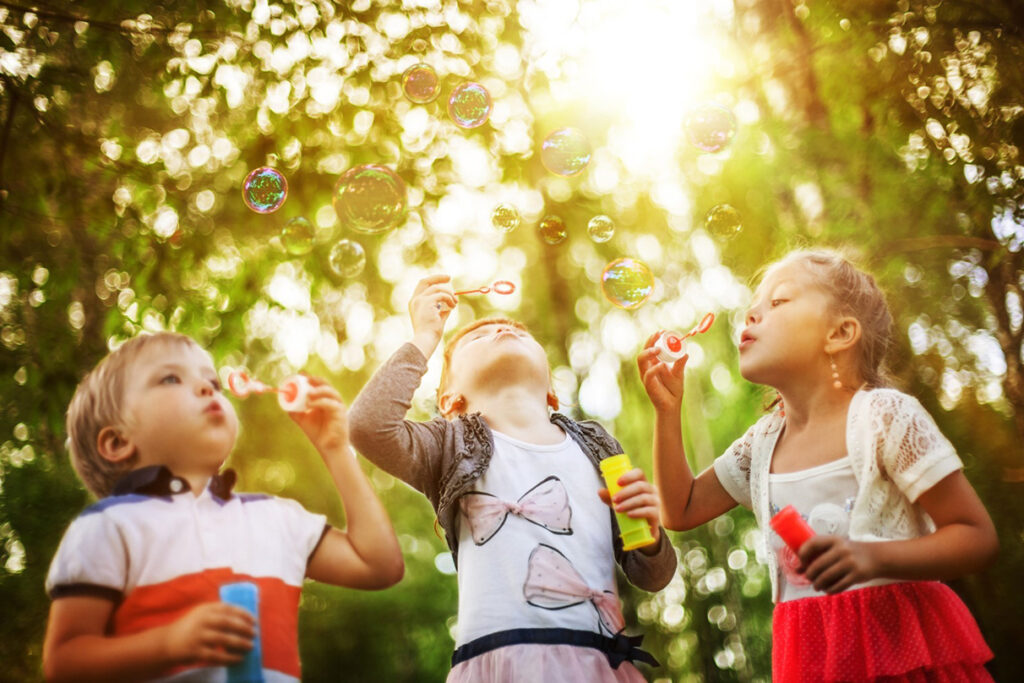 Three children blowing bubbles, yet another example of outdoor play