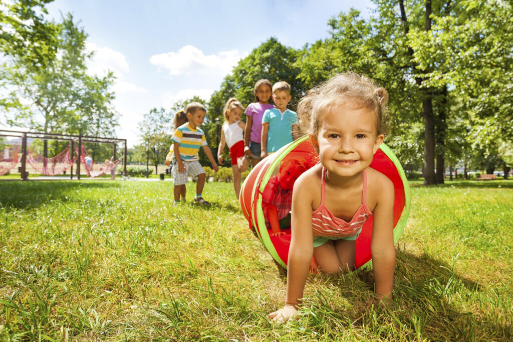 A young child crawling through a tunnel as other children wait their turn, a great example of outdoor play