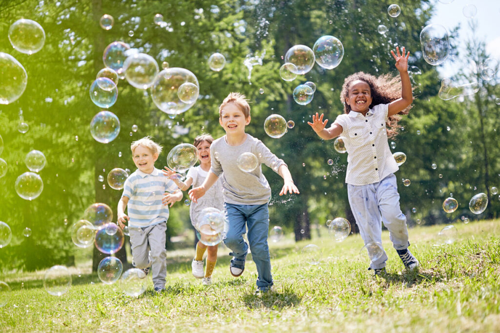 Several children running outside in a field, chasing bubbles, a good example of unstructured play