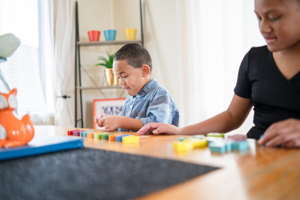 A mother and son play with blocks on a table. Each have their own blocks and are doing their own thing, helping to promote agency in early childhood