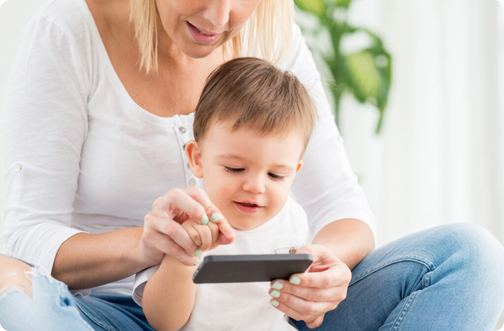 A woman and her baby touch a phone screen, perhaps signing their Comply Written Arrangement