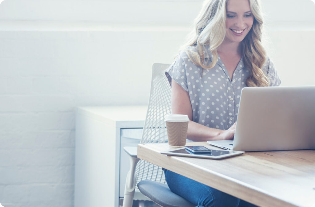 A woman smiles while she enters information on her laptop computer, perhaps a Complying Written Arrangement (CWA)