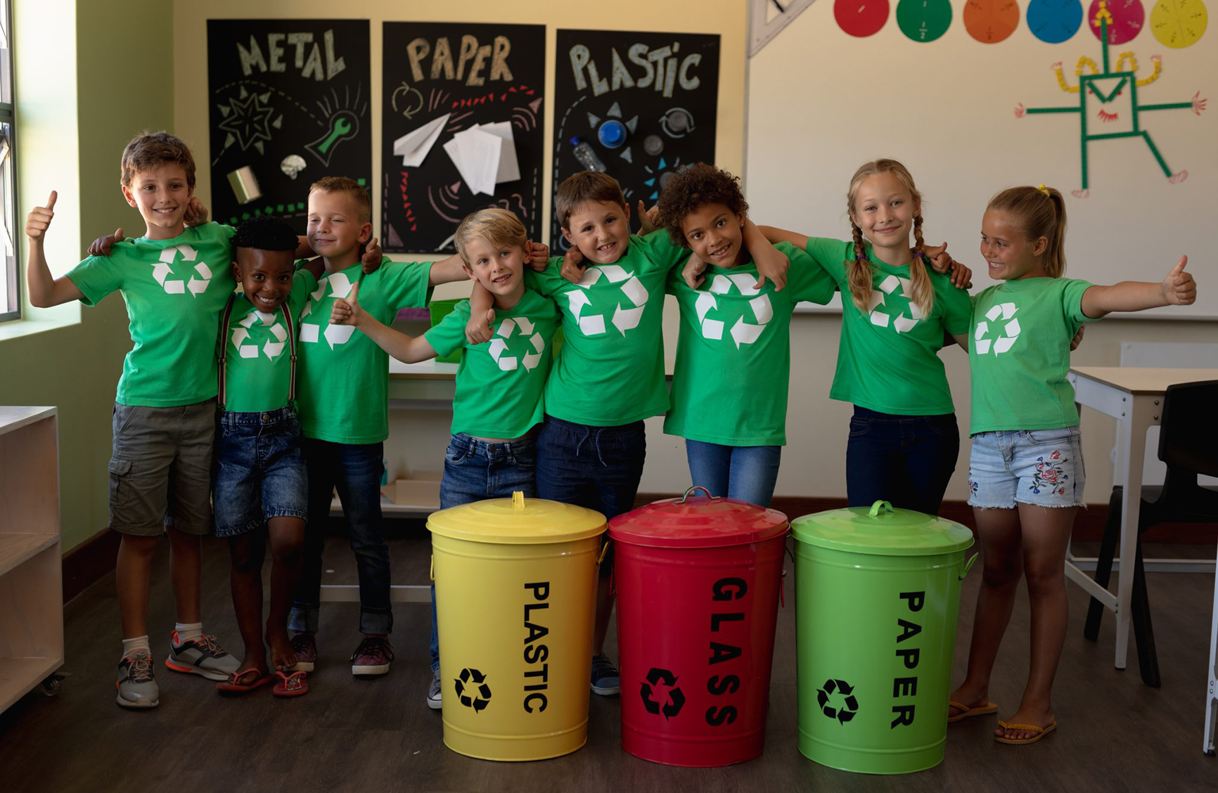 Children linking arms behind three recycling bins
