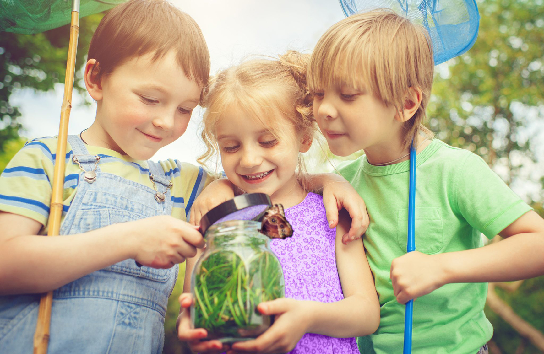 Three children engaging in outdoor play while looking at insects in a jar