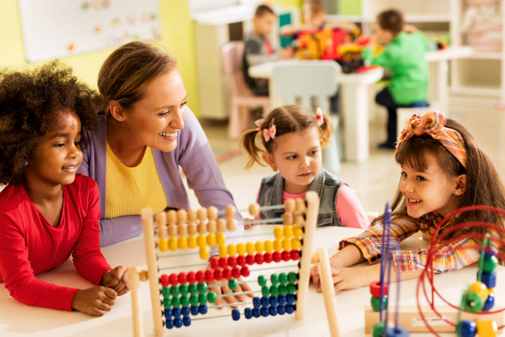 Three young girls sitting at a table with an educator, playing with an abacus