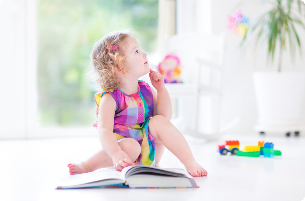 A little girl ponders the open book the floor in front of her, perhaps a children's book by an Australian author