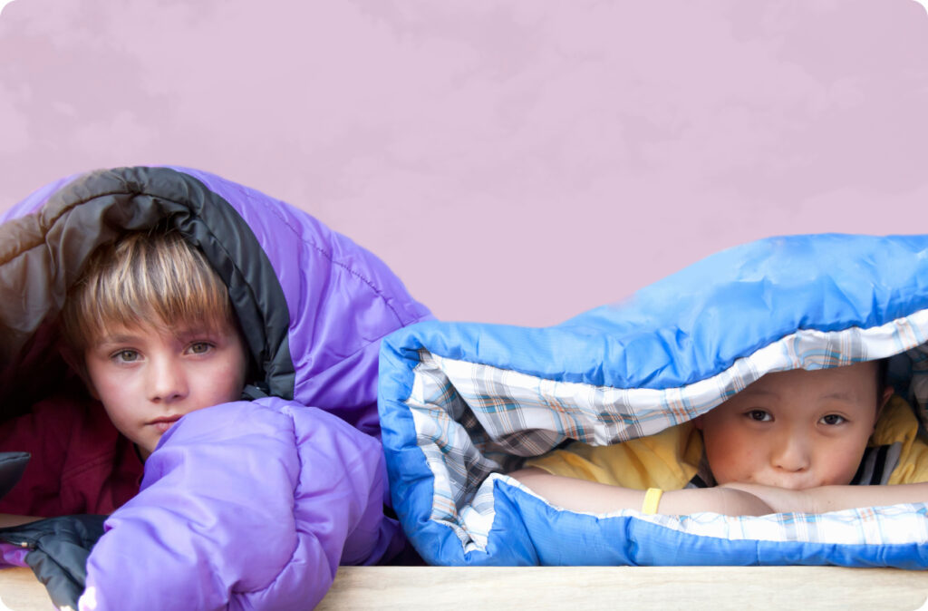 Too young children peaking out through the opening of their sleeping bags.