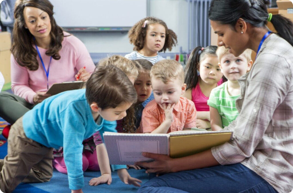 An ECE educator reading a book to young children while sitting on the floor