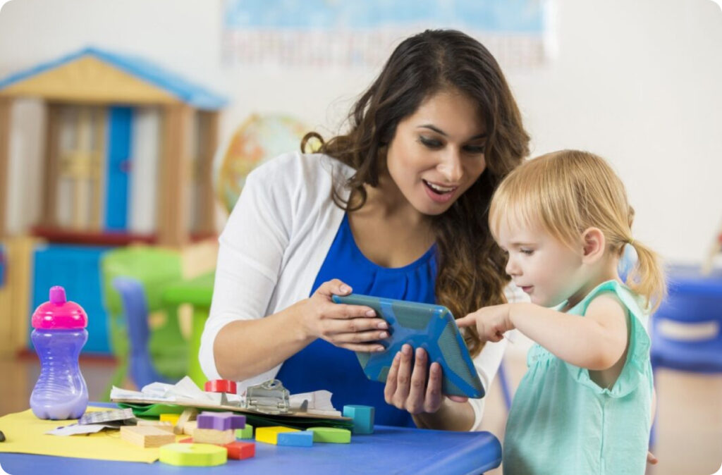 A young child touches a tablet held by a childcare educator, representing cyber security at your childcare service