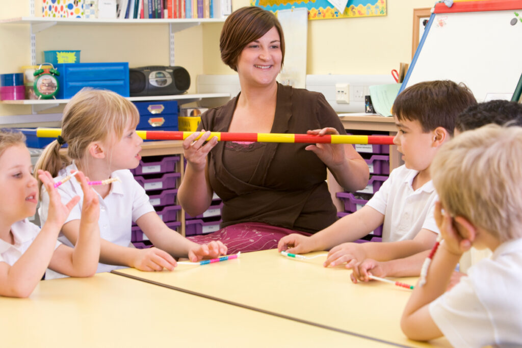 An educator sitting at a table, smiling as several young children
