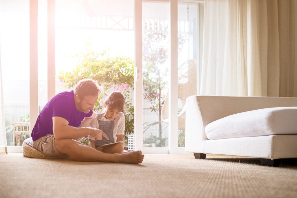 A father and daughter reading from a tablet while sitting on the floor