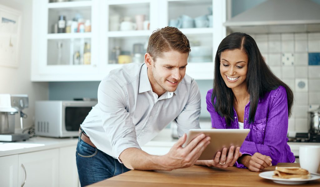 A man and a woman smile as they look at a tablet in their kitchen