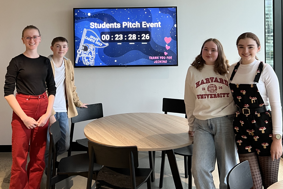 Students Evie, AJ, Sophia & Chili standing around a table, preparing for the Space Cadets pitch night