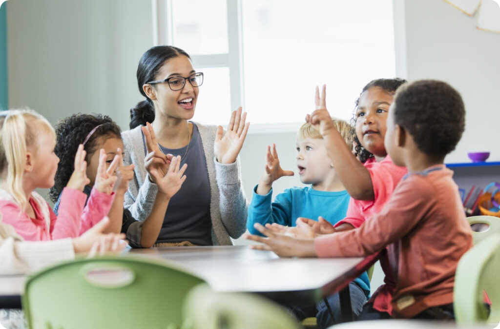 An educator sitting with six young children at a table, representing childcare staff shortages