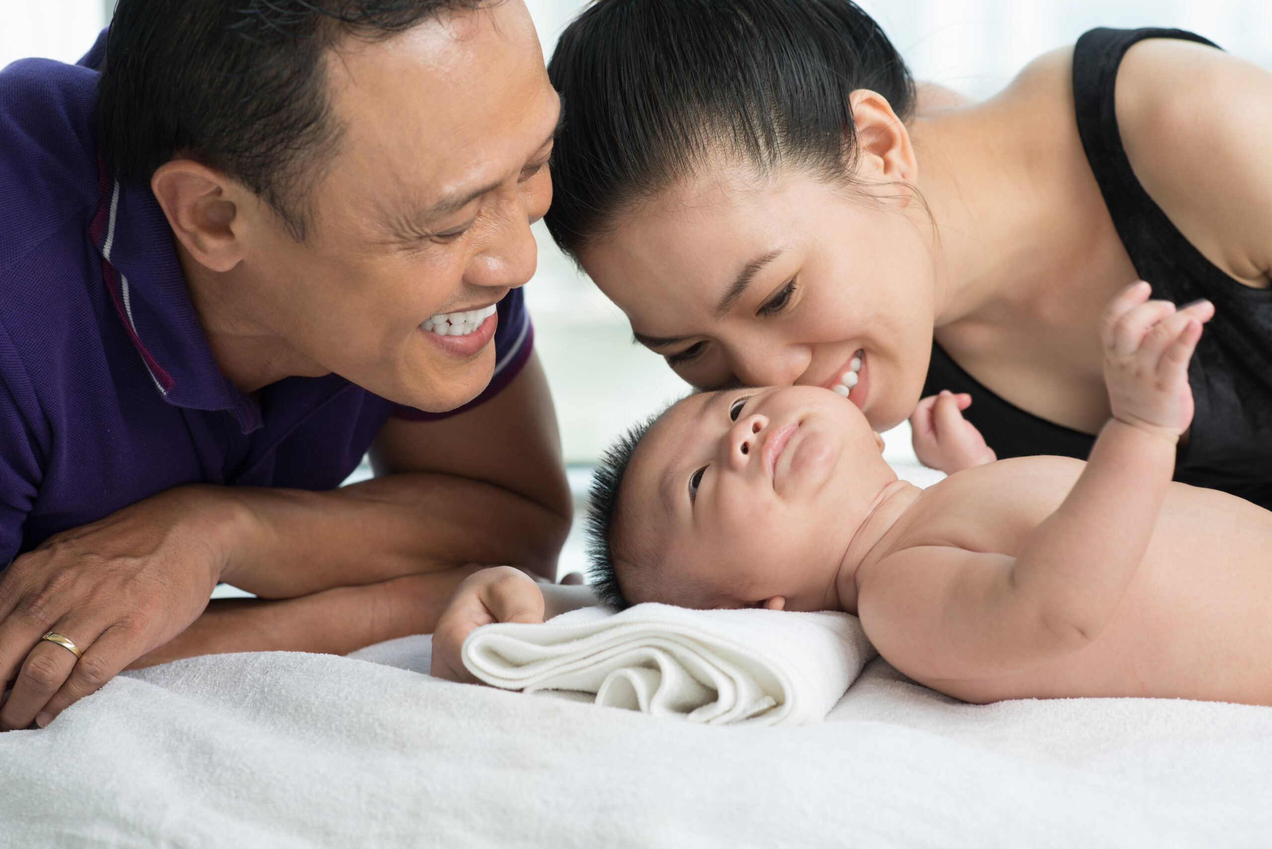 A father and mother smiling at their baby lying on her back