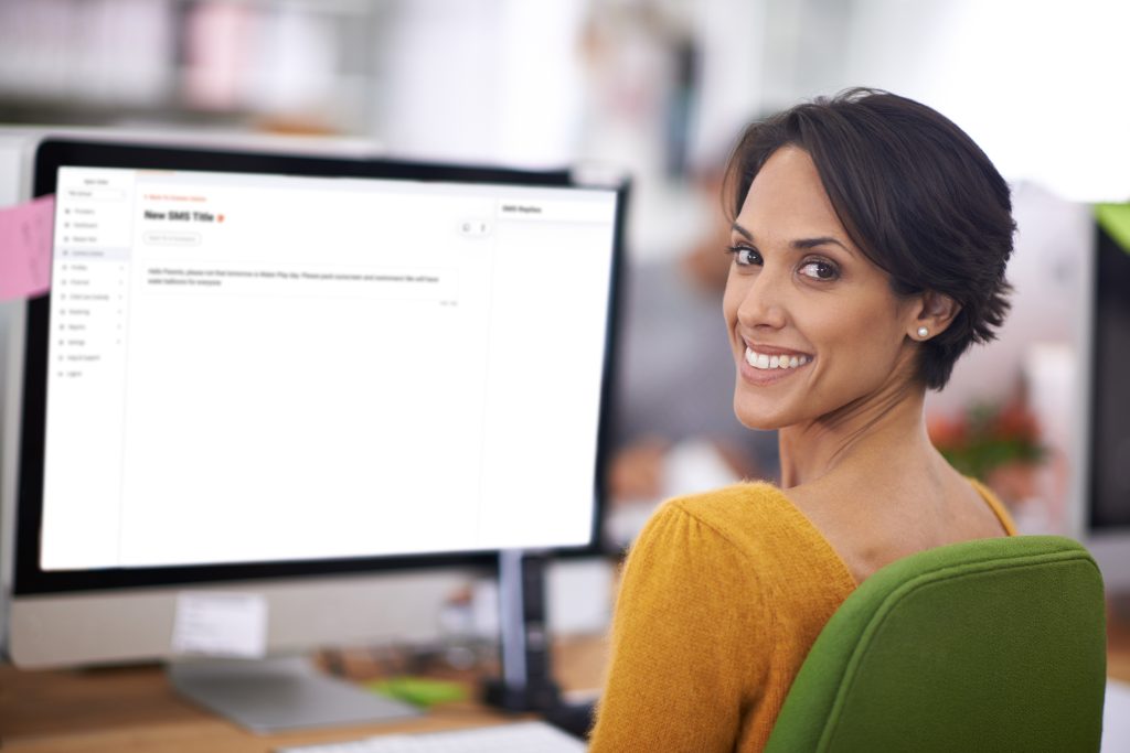 An educator smiling at the camera with the Office SMS interface blurred in the background.