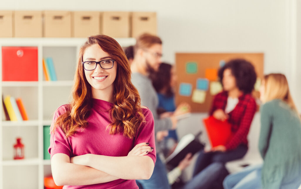 An educator smiles at the camera with her colleagues blurred in the background.