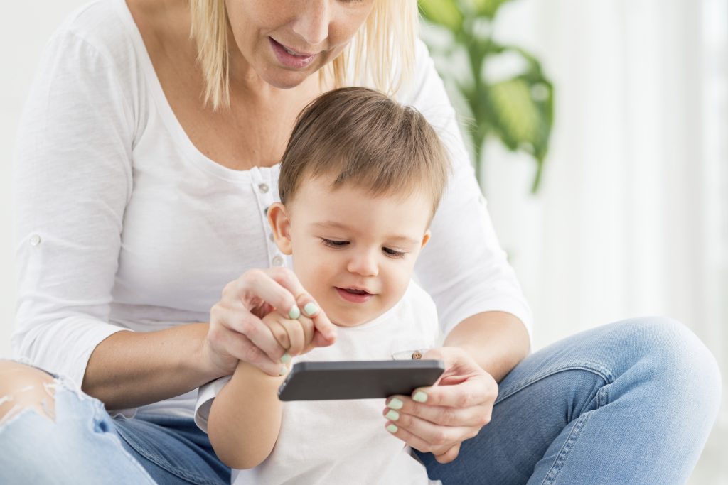A toddler and his mother read an SMS message on a mobile phone.