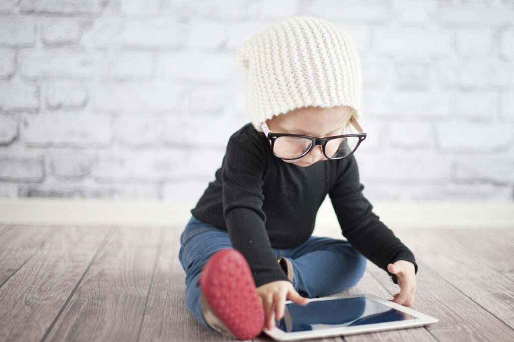 A young child, wearing glasses, starting at a tablet, perhaps looking at a centralised booking manager for ECEC