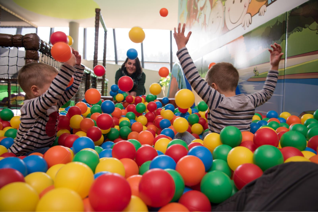 Children play in a ball pool while an educator looks on, perhaps gathering documentation for a milestone-based summative assessment