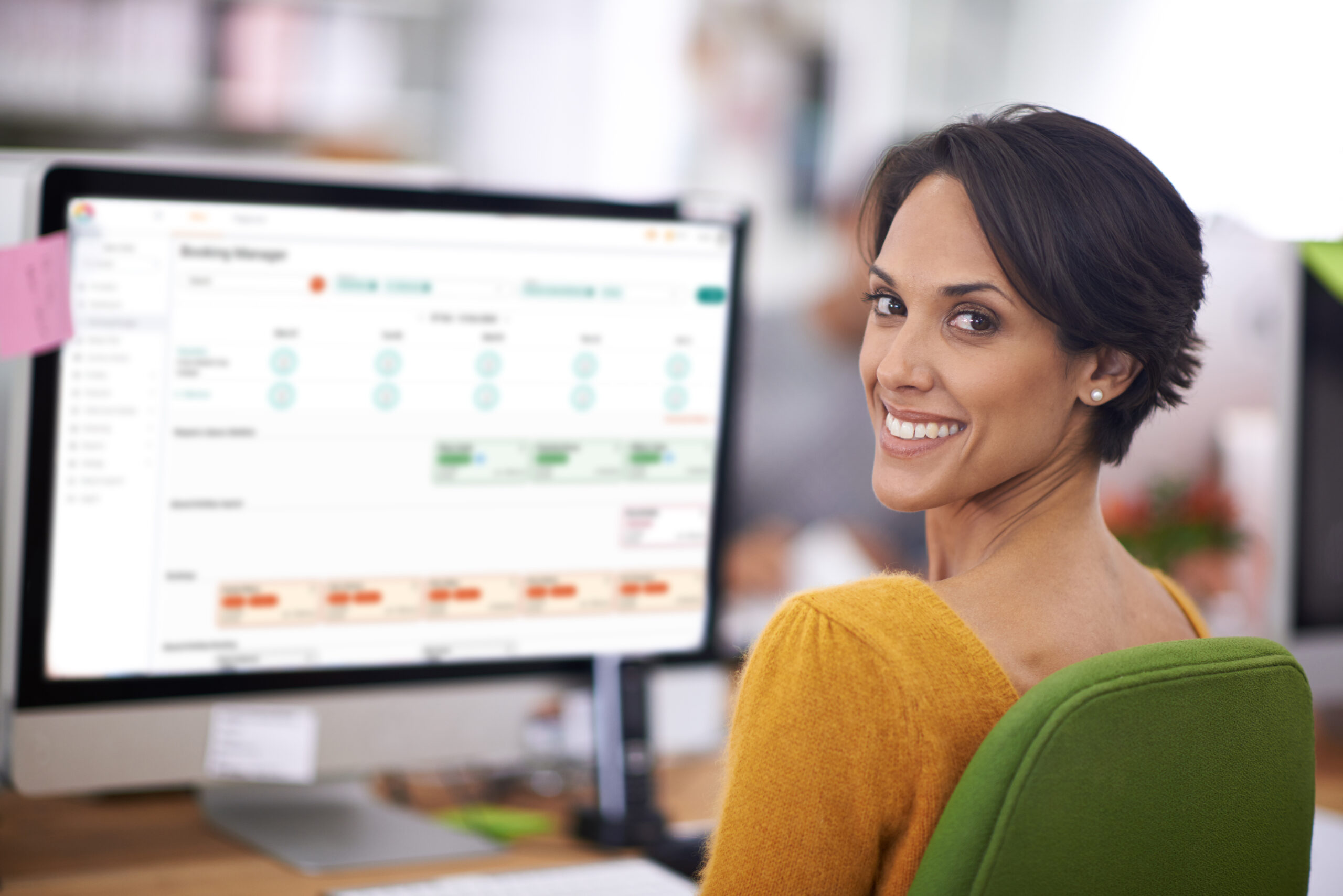 A woman looking over her shoulder at the camera with the Office dashboard on the screen in the background, displaying digital enrolments