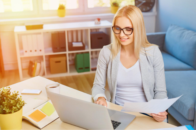 A young woman sitting at a laptop, holding papers, perhaps reviewing digital enrolments
